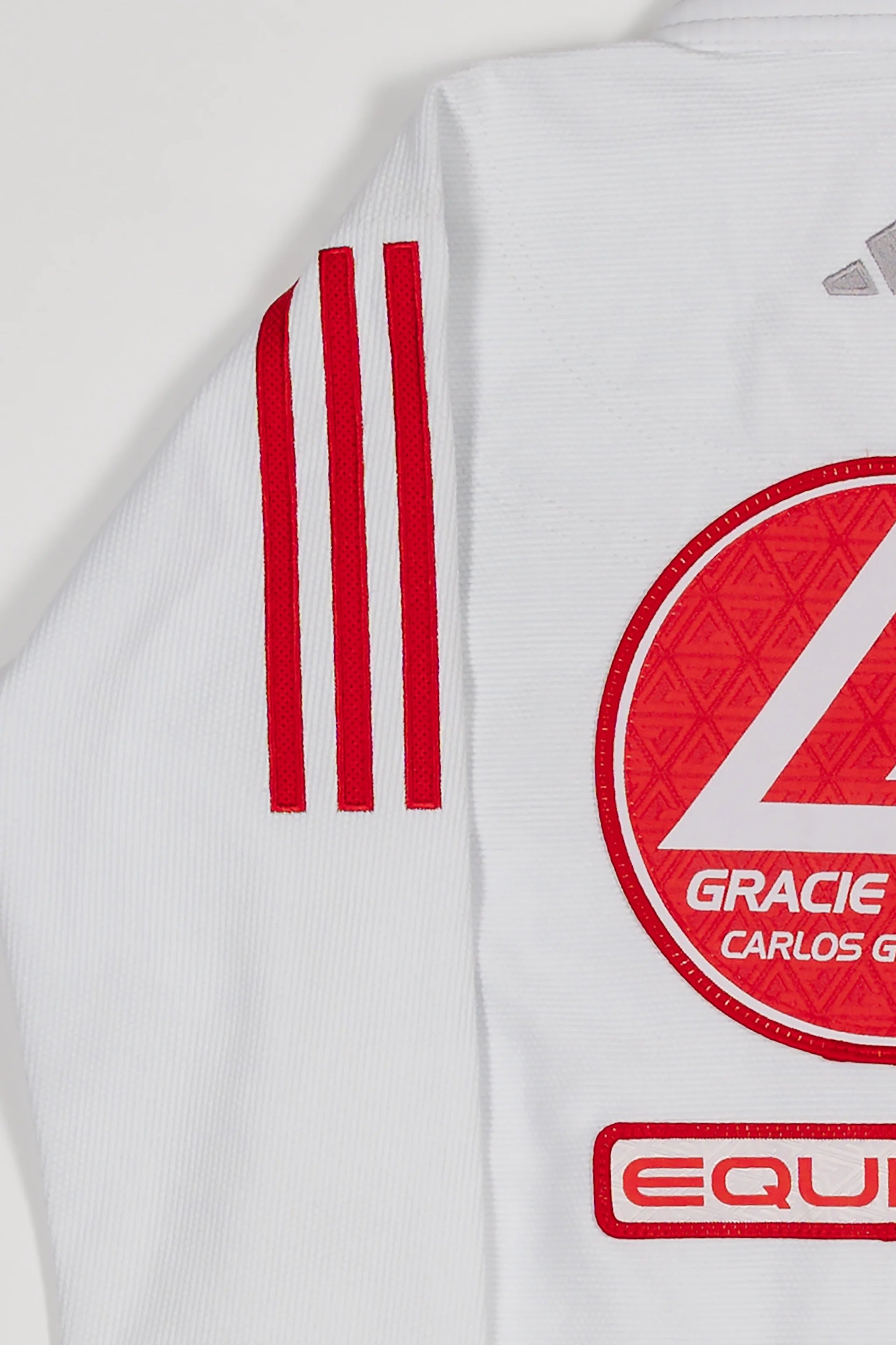 Close-up of white GB x adidas III Stripes Youth Kimono shoulder and back showing red 3-Stripes detail, Red Shield patch, and red EQUIPE GB patch embroidery.