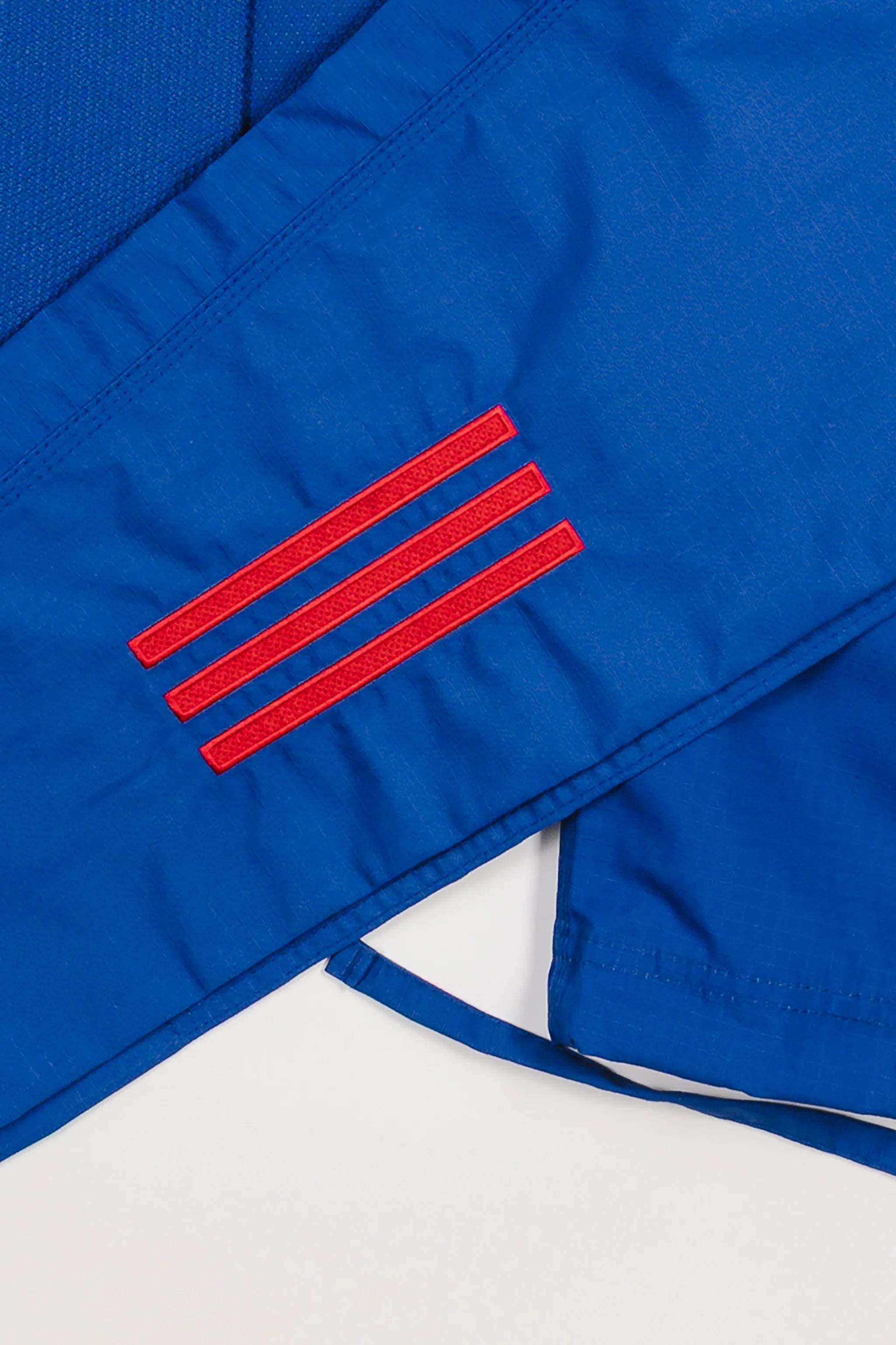 Close-up of blue GB x adidas III Stripes Women’s Kimono pants showing embroidered red 3-Stripes detail on lightweight ripstop fabric.
