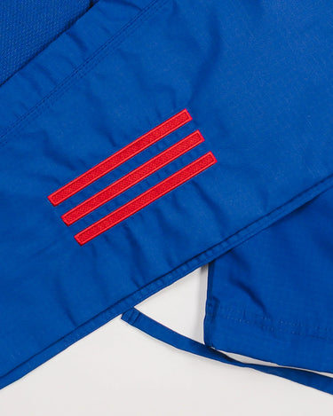 Close-up of blue GB x adidas III Stripes Women’s Kimono pants showing embroidered red 3-Stripes detail on lightweight ripstop fabric.