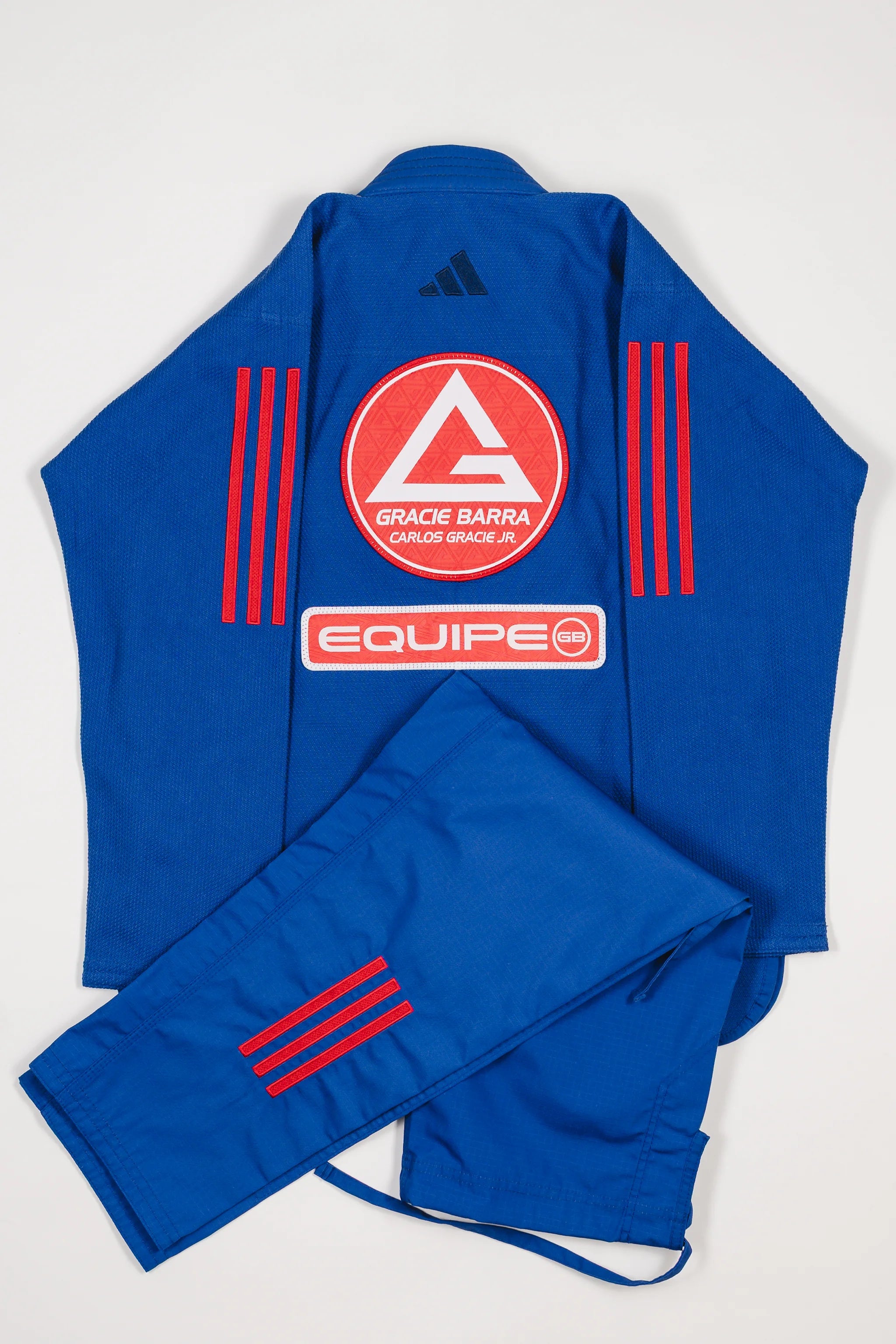 Back view of blue GB x adidas III Stripes Women’s Kimono with pants folded across jacket, featuring large Red Shield patch, red EQUIPE GB patch, and bold red 3-Stripes on shoulders and pant leg.