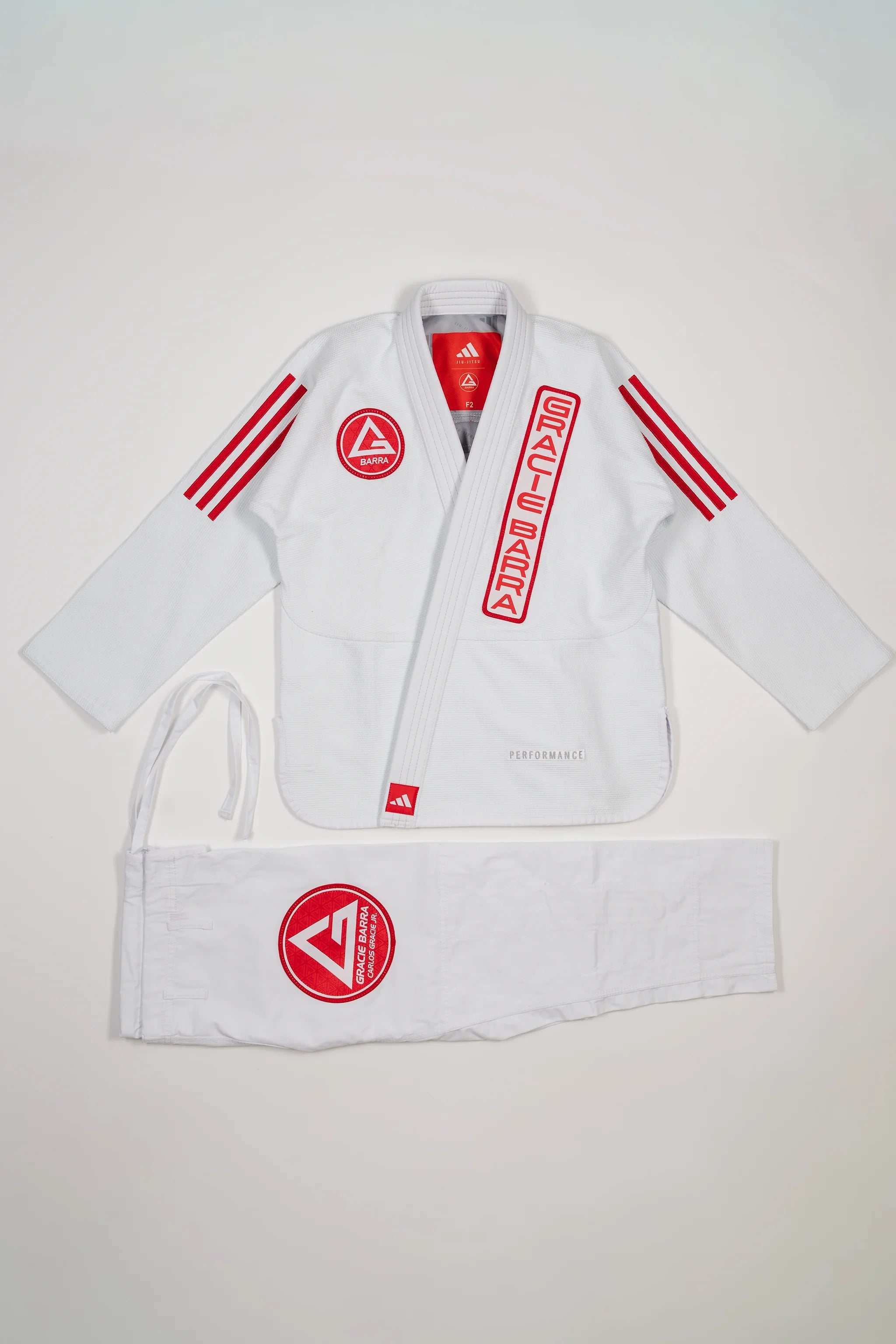 White GB x adidas III Stripes Women’s Kimono laid flat on white background, featuring bold red 3-Stripes on shoulders, red Barra Shield on chest, and Gracie Barra lapel patch with adidas Performance embroidery.