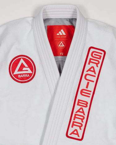 Close-up of white GB x adidas III Stripes Women’s Kimono jacket showing red Barra Shield on chest, Gracie Barra lapel patch, and adidas Jiu-Jitsu label inside collar.