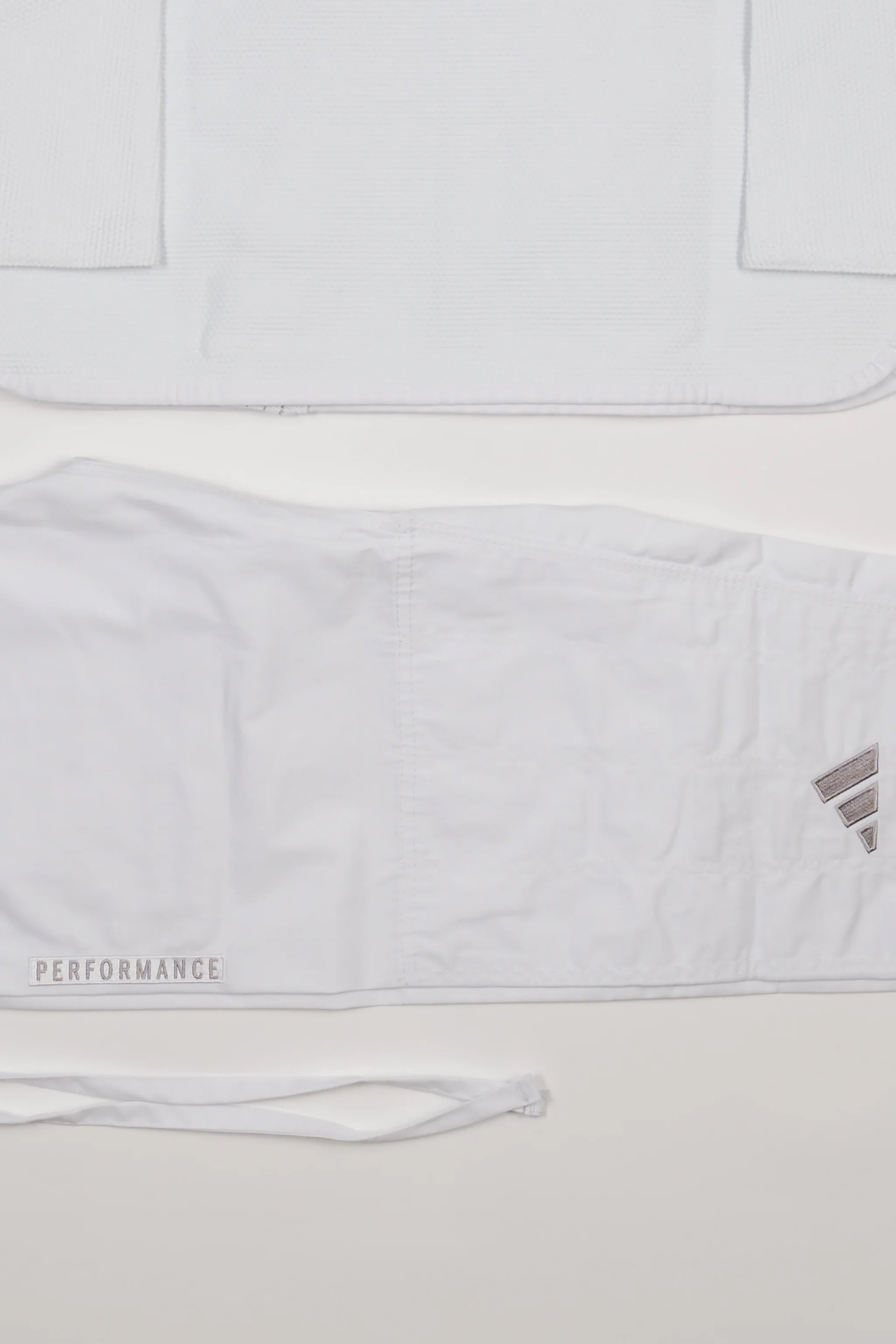 Detail view of white GB x adidas III Stripes Women’s Kimono jacket and pants on white background, showing embroidered adidas logo and tonal Performance text on pant leg.