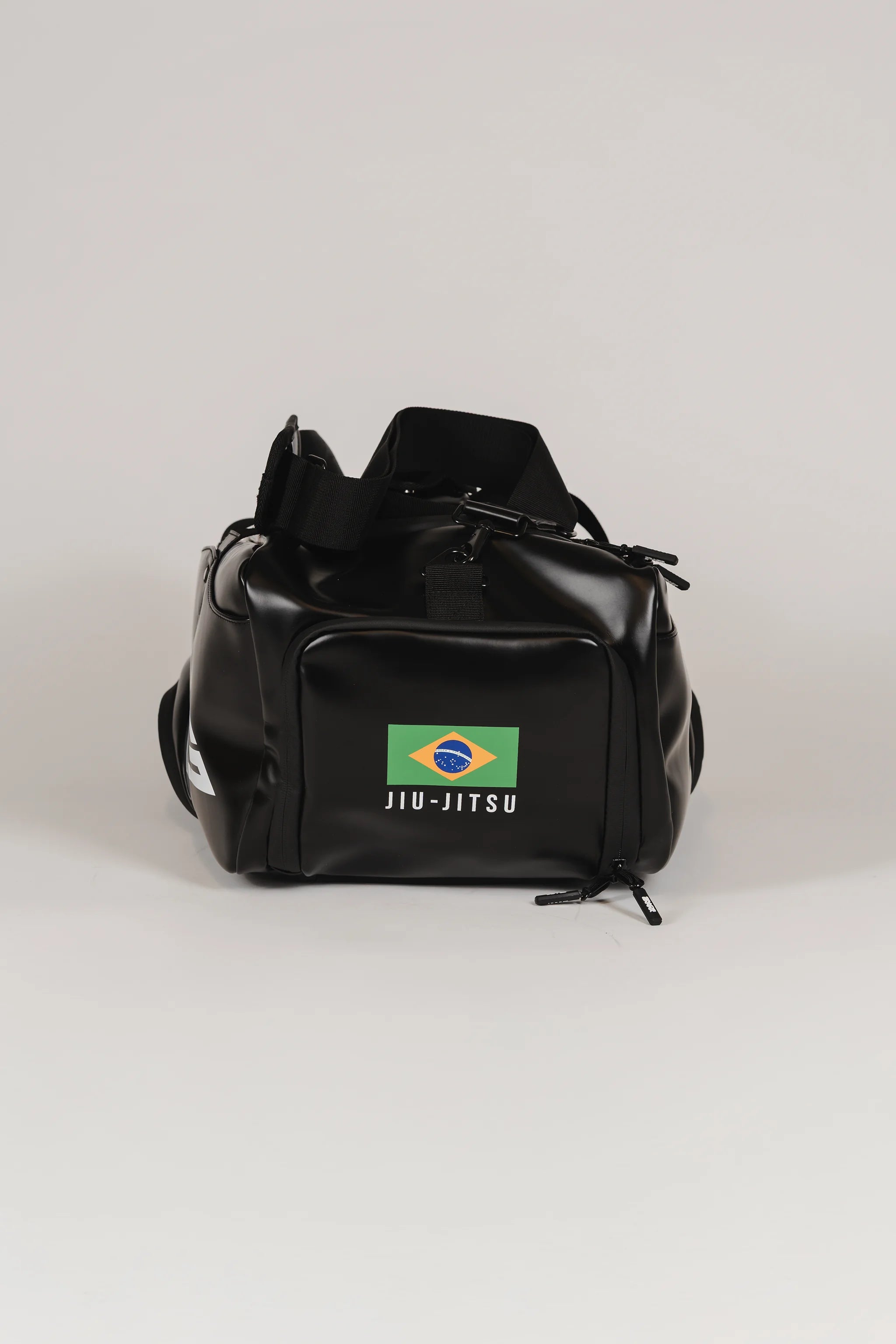 Front view of the black Legacy Travel Duffel on a light gray background, featuring the Brazil flag patch with ‘Jiu-Jitsu’ text and a zippered front compartment.