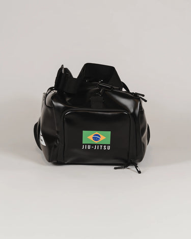 Front view of the black Legacy Travel Duffel on a light gray background, featuring the Brazil flag patch with ‘Jiu-Jitsu’ text and a zippered front compartment.