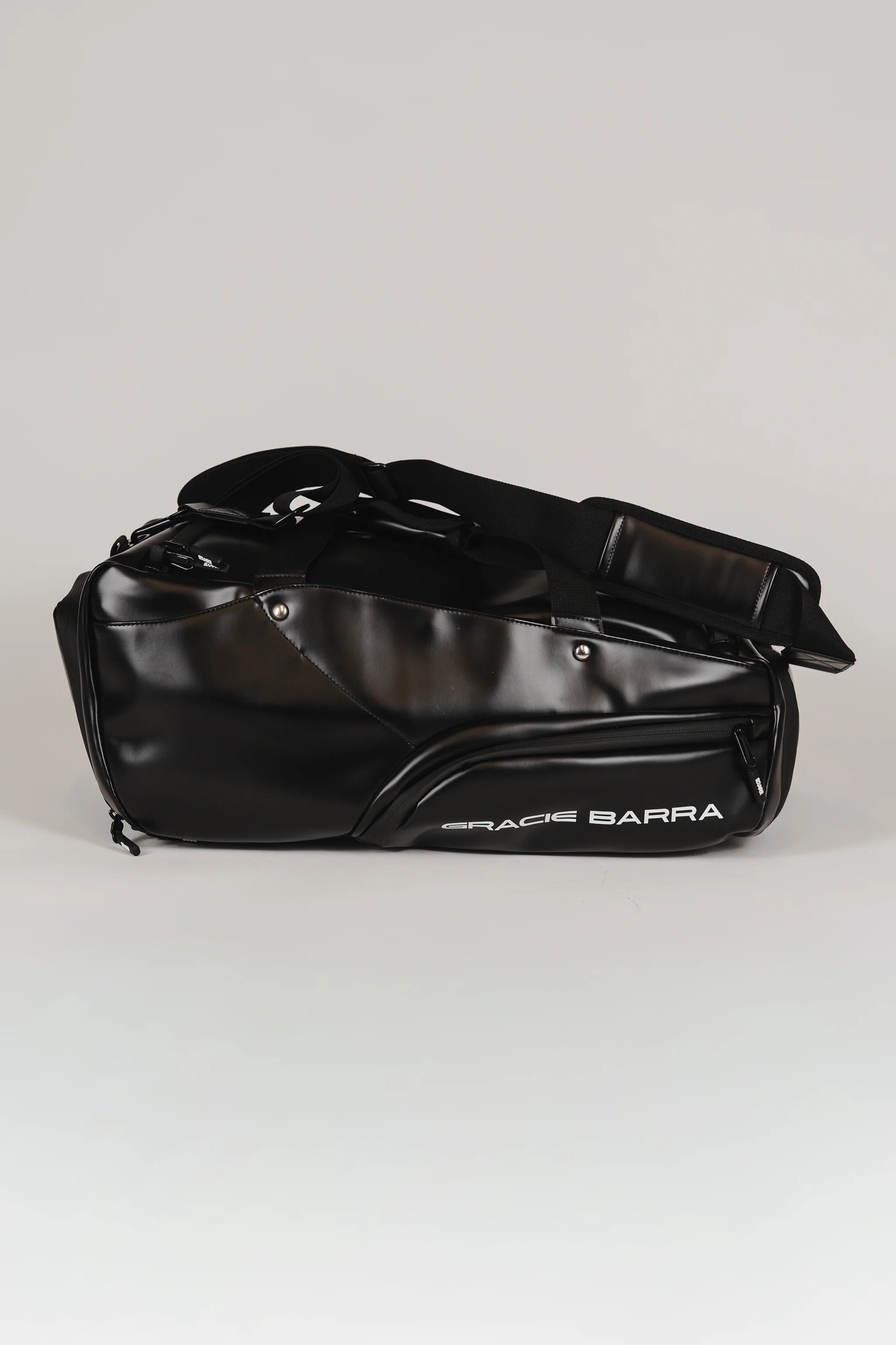 Side view of the black Legacy Travel Duffel on a light gray background, showing the ‘Gracie Barra’ wordmark and the streamlined exterior pocket design.