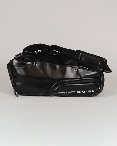 Side view of the black Legacy Travel Duffel on a light gray background, showing the ‘Gracie Barra’ wordmark and the streamlined exterior pocket design.