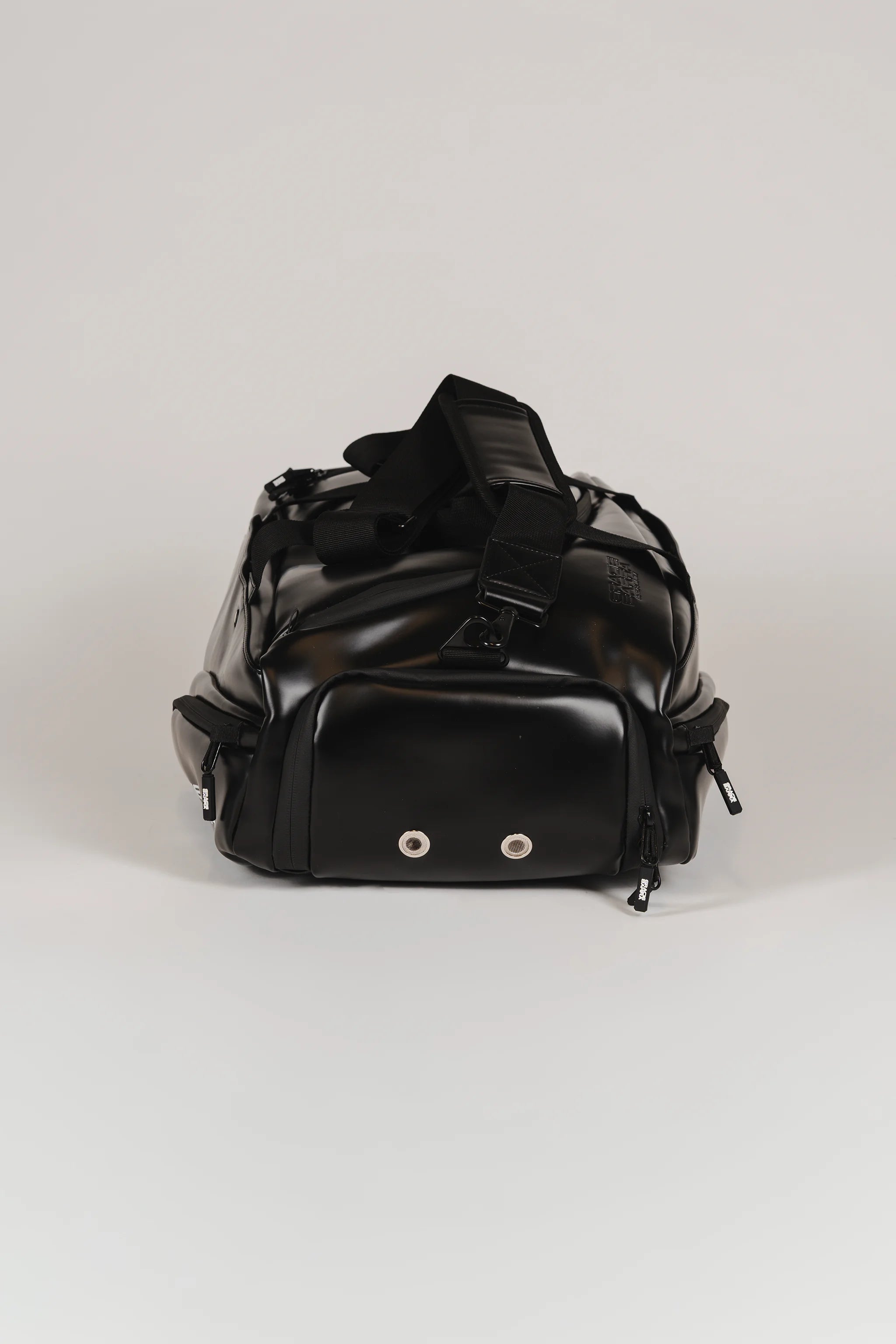 End view of the black Legacy Travel Duffel on a light gray background, showing the ventilated compartment panel with two metal eyelets and the padded shoulder strap.