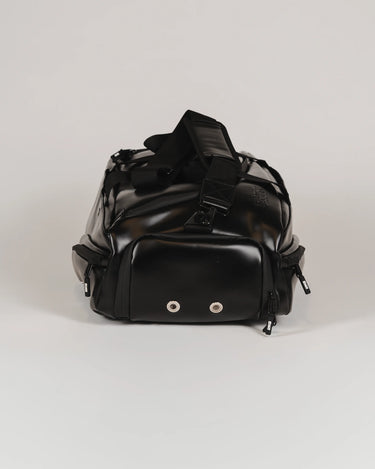 End view of the black Legacy Travel Duffel on a light gray background, showing the ventilated compartment panel with two metal eyelets and the padded shoulder strap.