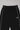 Front detail of black Legacy Windrunner pants featuring white side piping and the Legacy G logo on the thigh, photographed on a light gray background.