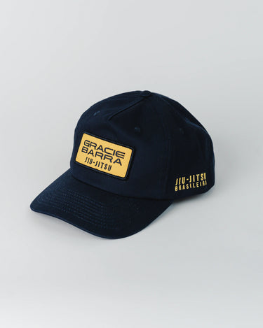 Navy blue Gracie Barra Lutador Cap with gold embroidered patch on front reading “Gracie Barra Jiu-Jitsu” and additional gold “Jiu-Jitsu Brasileiro” text on the side.