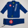 Blue Lutador Kimono set laid flat on a light gray background, featuring the pearl-weave jacket with Gracie Barra patches and embroidery, and matching ripstop pants with the Lutador wordmark and red Barra Shield.