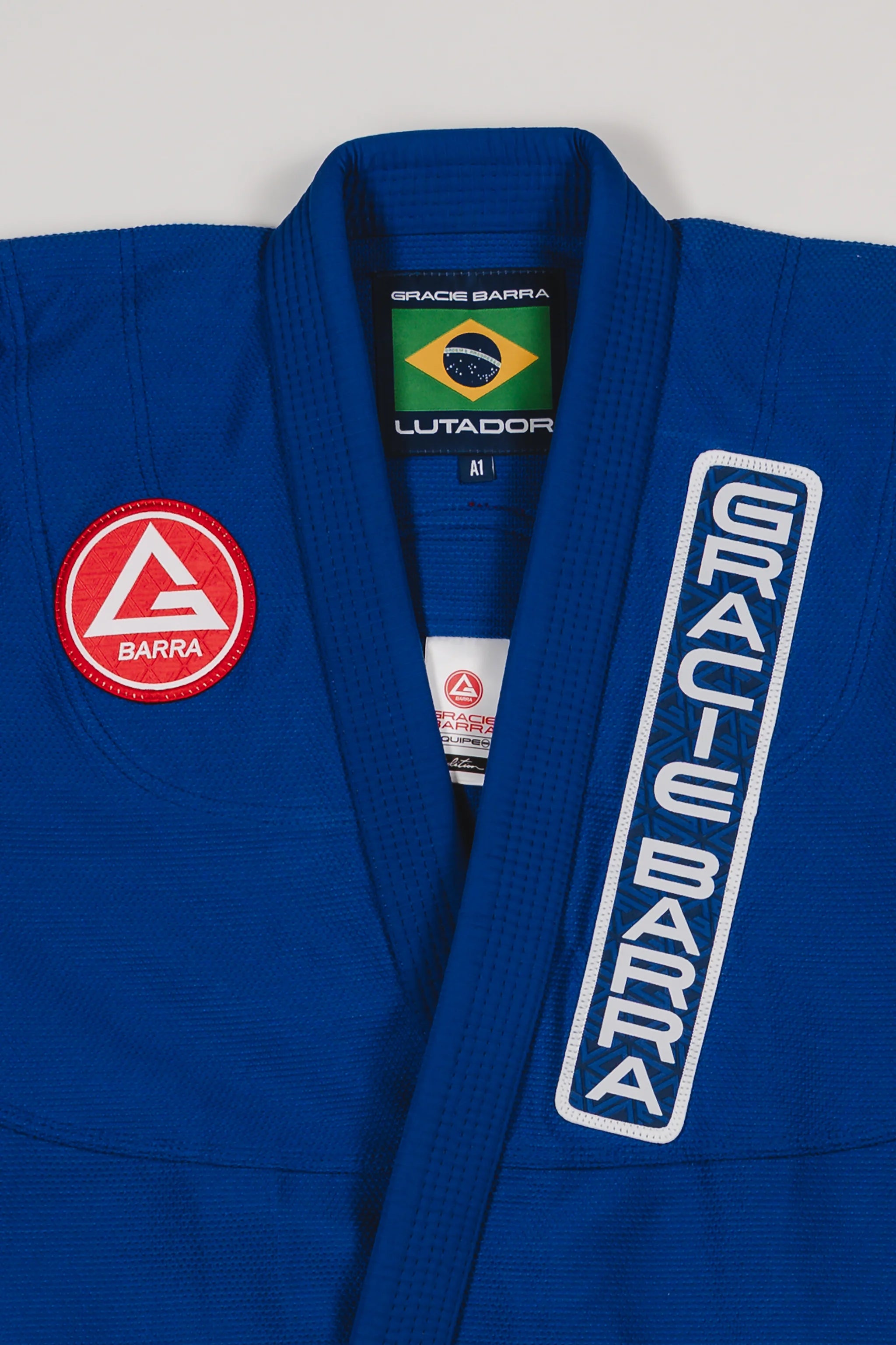 Close-up of the blue Lutador Kimono jacket showing the embroidered Gracie Barra chest patch, vertical Gracie Barra lapel embroidery, and Brazilian flag collar label.
