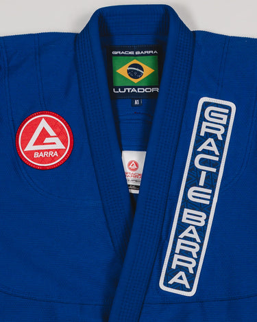 Close-up of the blue Lutador Kimono jacket showing the embroidered Gracie Barra chest patch, vertical Gracie Barra lapel embroidery, and Brazilian flag collar label.