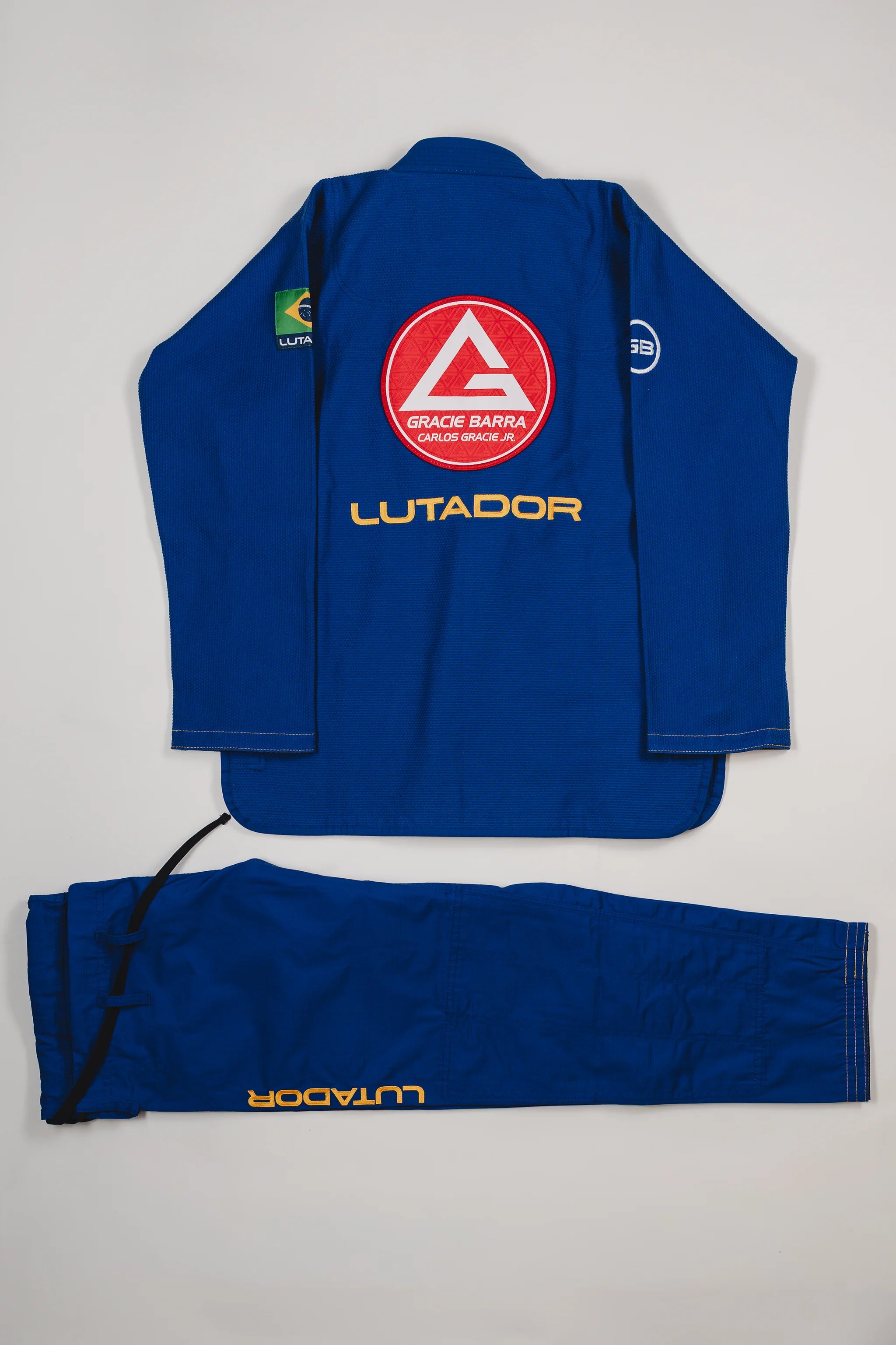 Back view of the blue Lutador Kimono jacket and pants laid flat on a light gray background, featuring the large red Barra Shield, gold Lutador embroidery, and matching pant branding.
