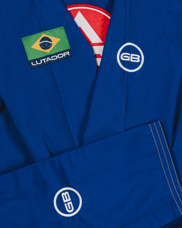 Close-up of the blue Lutador Kimono showing the Brazilian flag Lutador patch, white GB circle logos on the sleeve and pant leg, and textured pearl-weave fabric.