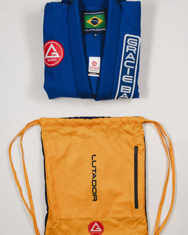 Folded blue Lutador Kimono jacket displayed above the yellow Lutador drawstring bag, both showing Gracie Barra branding on a light gray background.