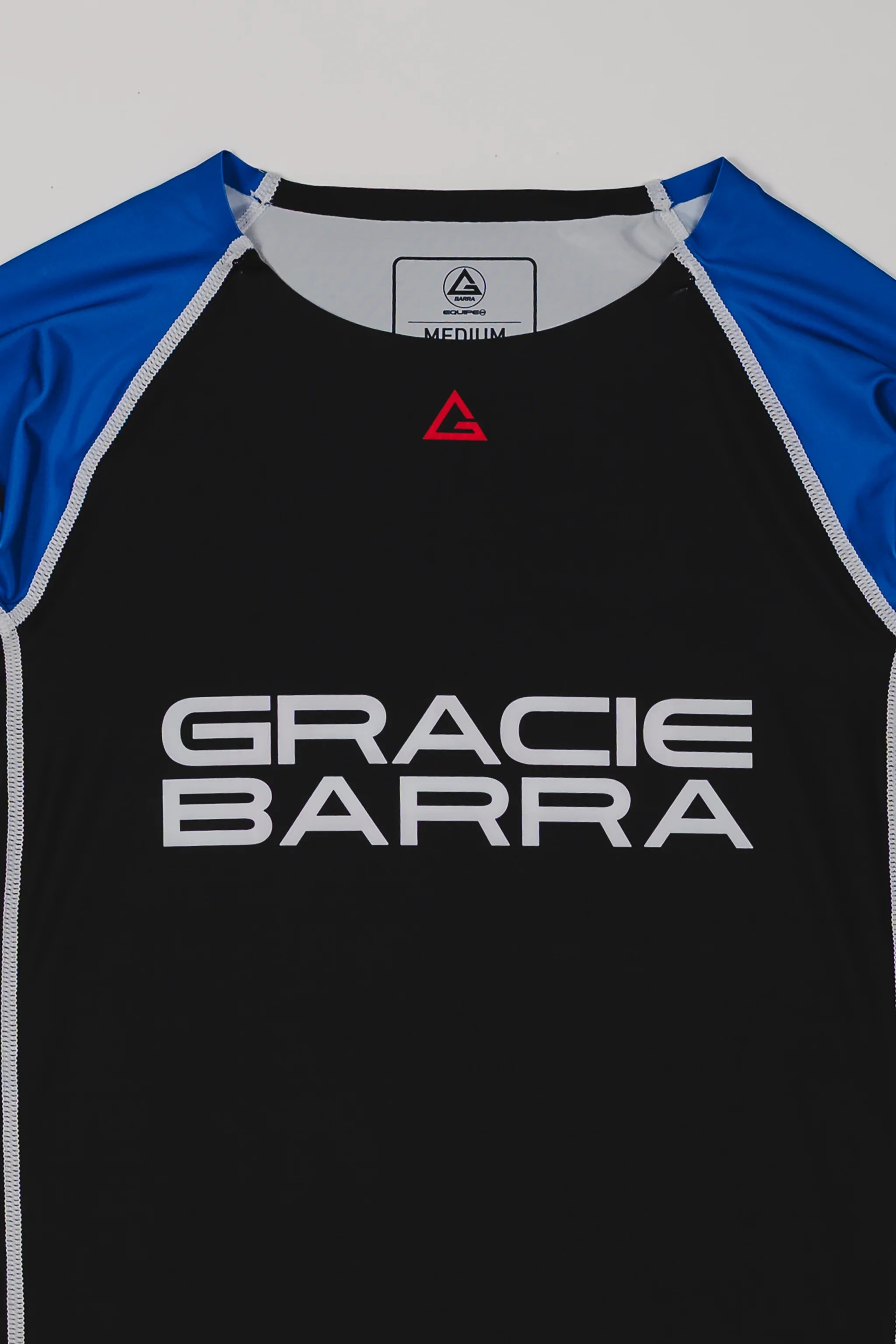 Close-up of the Lutador Longsleeve Ranked Rashguard in blue, showing the black torso, blue raglan sleeves, red Legacy G chest logo, and large white Gracie Barra wordmark.