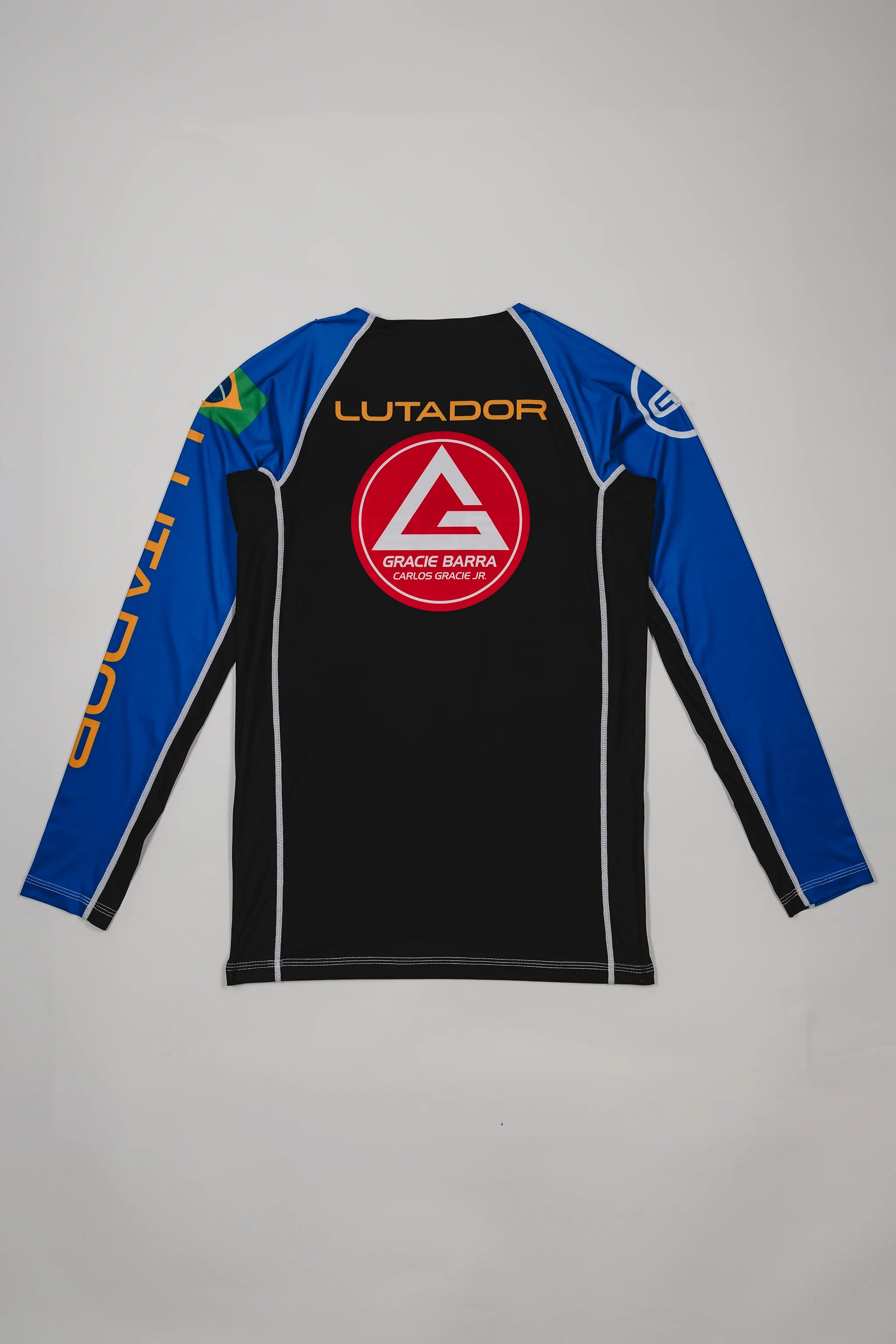 Back view of the Lutador Longsleeve Ranked Rashguard in blue, showing the large red Barra Shield, gold ‘Lutador’ text, Brazilian flag sleeve patch, and contrasting black torso panel.