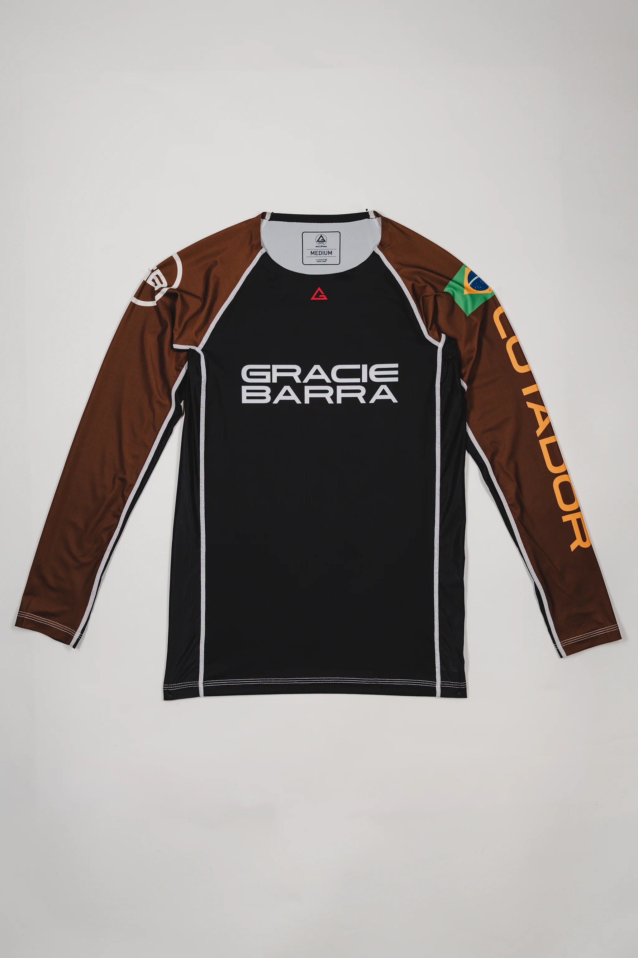 Full front view of the Lutador Longsleeve Ranked Rashguard in brown, featuring the black torso, brown raglan sleeves, Gracie Barra wordmark, Brazilian flag arm patch, and gold ‘Lutador’ sleeve print.