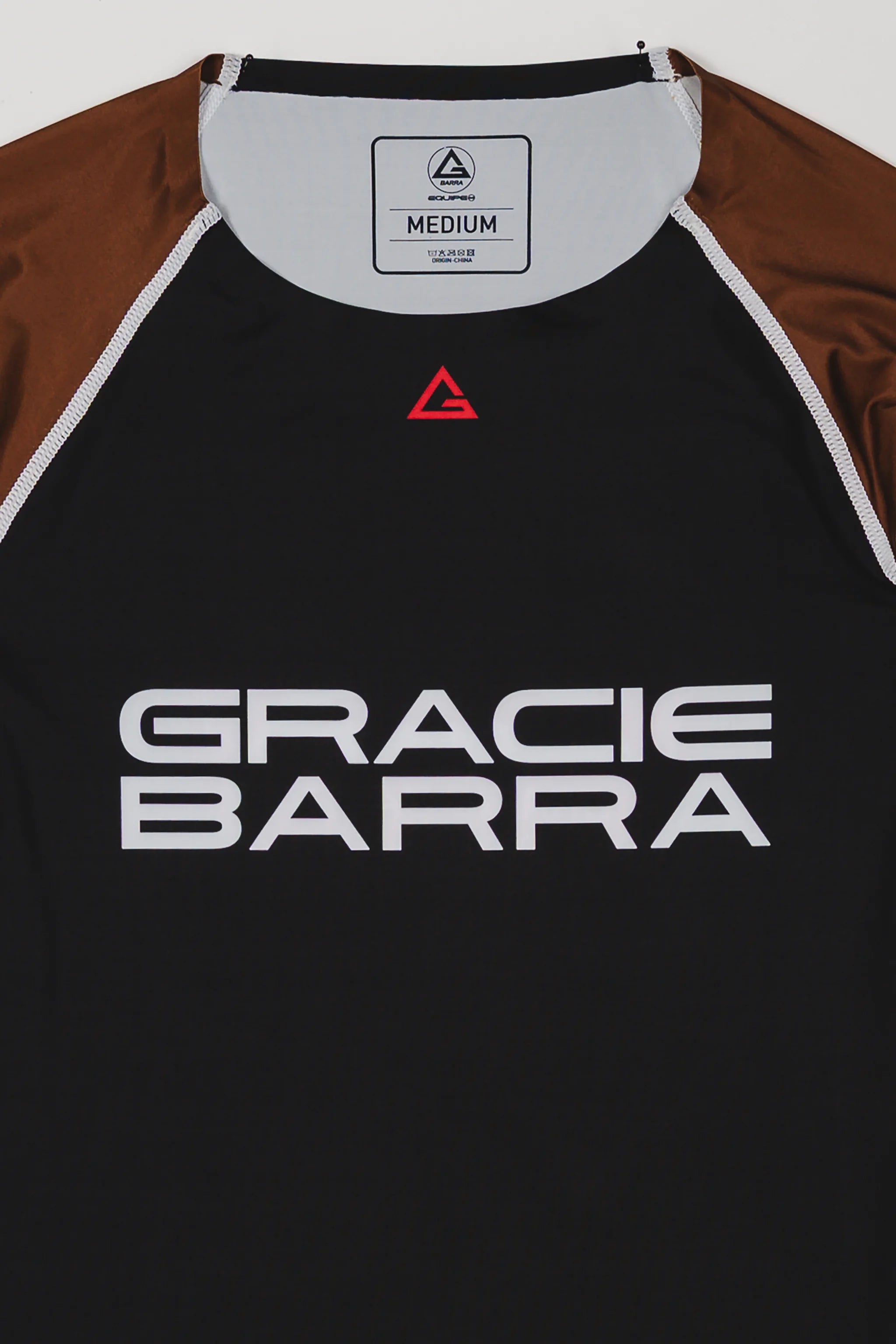 Close-up of the Lutador Longsleeve Ranked Rashguard in brown, showing the black torso, brown raglan sleeves, red Legacy G chest logo, and large white Gracie Barra wordmark.