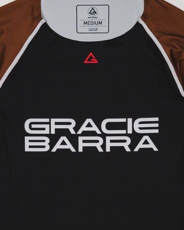 Close-up of the Lutador Longsleeve Ranked Rashguard in brown, showing the black torso, brown raglan sleeves, red Legacy G chest logo, and large white Gracie Barra wordmark.