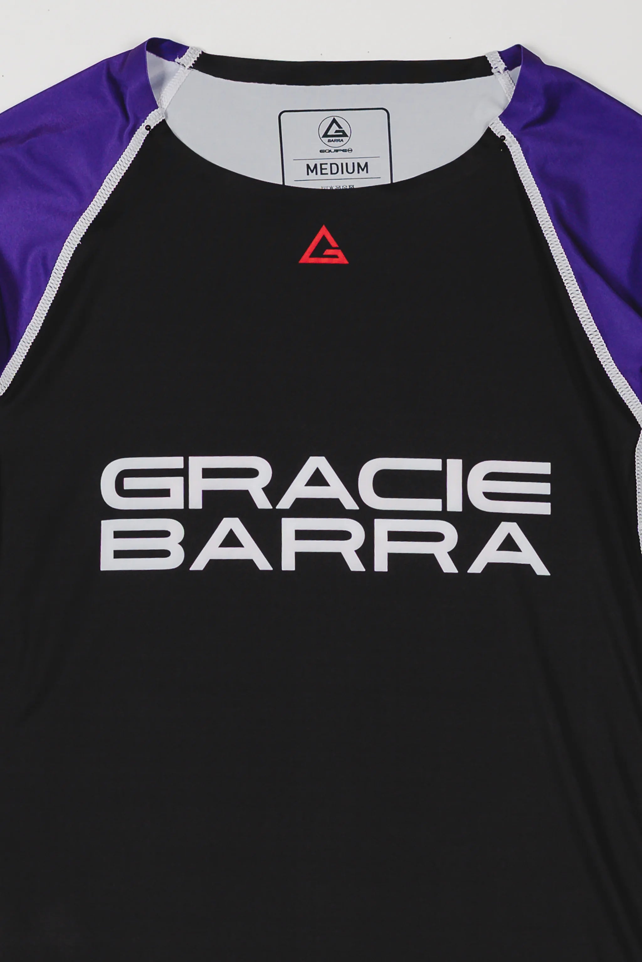 Close-up of the Lutador Longsleeve Ranked Rashguard in purple, showing the black torso, purple raglan sleeves, red Legacy G chest logo, and large white Gracie Barra wordmark.