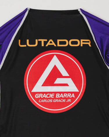 Close-up of the back of the Lutador Longsleeve Ranked Rashguard in purple, showing the gold ‘Lutador’ text and large red Barra Shield on the black panel with purple sleeves.