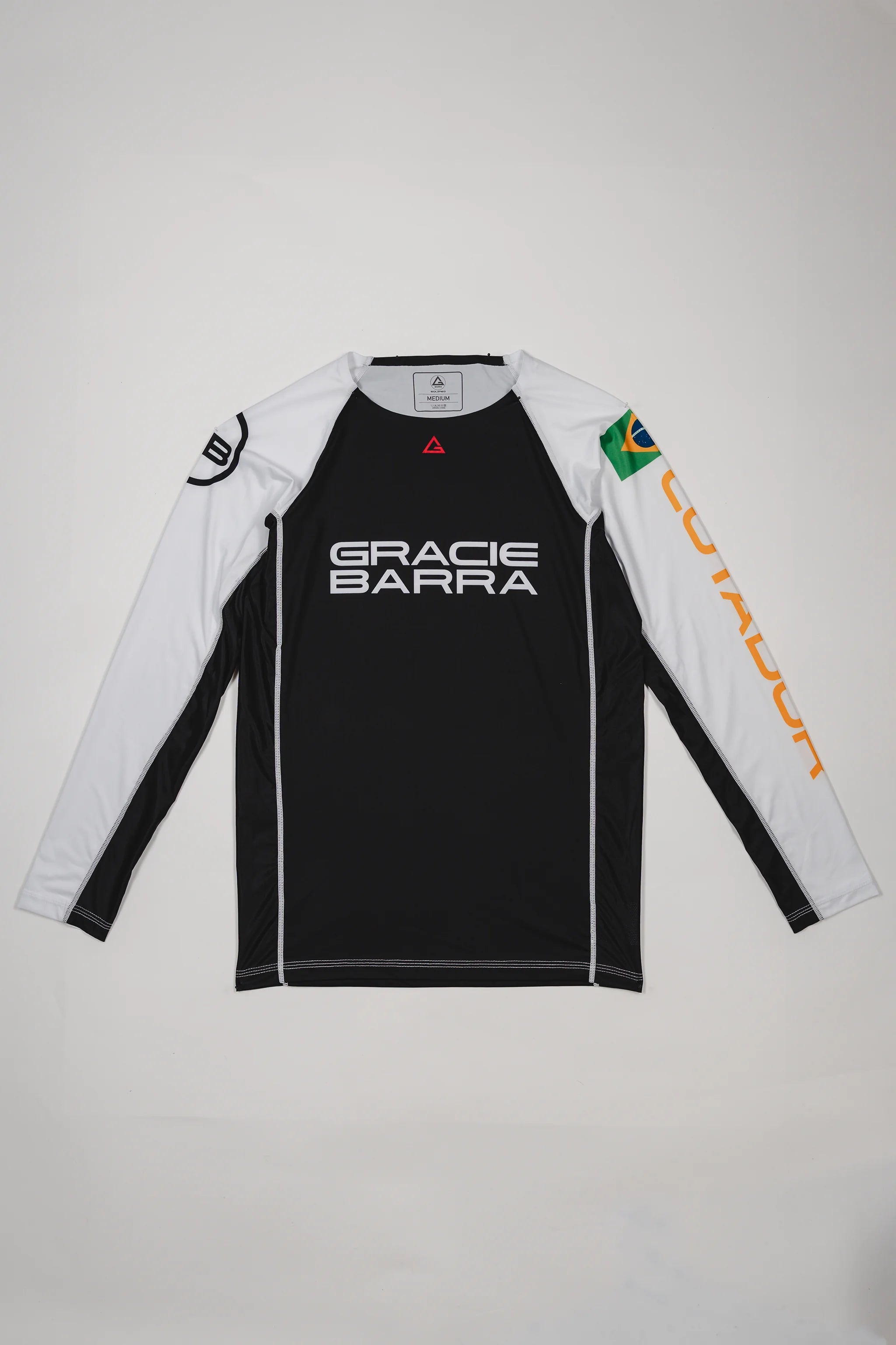 Full front view of the Lutador Longsleeve Ranked Rashguard laid flat, showing black torso, white raglan sleeves, Gracie Barra wordmark, Brazilian flag arm patch, and gold ‘Lutador’ sleeve print.