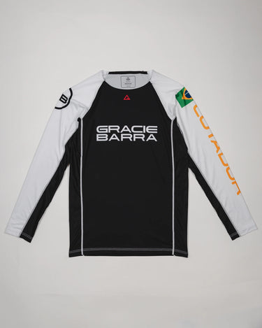 Full front view of the Lutador Longsleeve Ranked Rashguard laid flat, showing black torso, white raglan sleeves, Gracie Barra wordmark, Brazilian flag arm patch, and gold ‘Lutador’ sleeve print.
