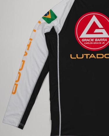 Angled back view of the Lutador Longsleeve Ranked Rashguard showing the red Barra Shield, gold ‘Lutador’ text, Brazilian flag sleeve patch, and white raglan sleeve with gold lettering.