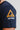 Close-up of the gold Gracie Barra triangle logo and white Equipe GB badge printed on the sleeve of the navy Lutador mens tee.