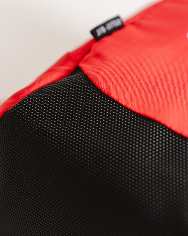 Close-up of Red Comp GB4 Backpack base showing black reinforced bottom panel with textured finish and woven GB4 label for durability.