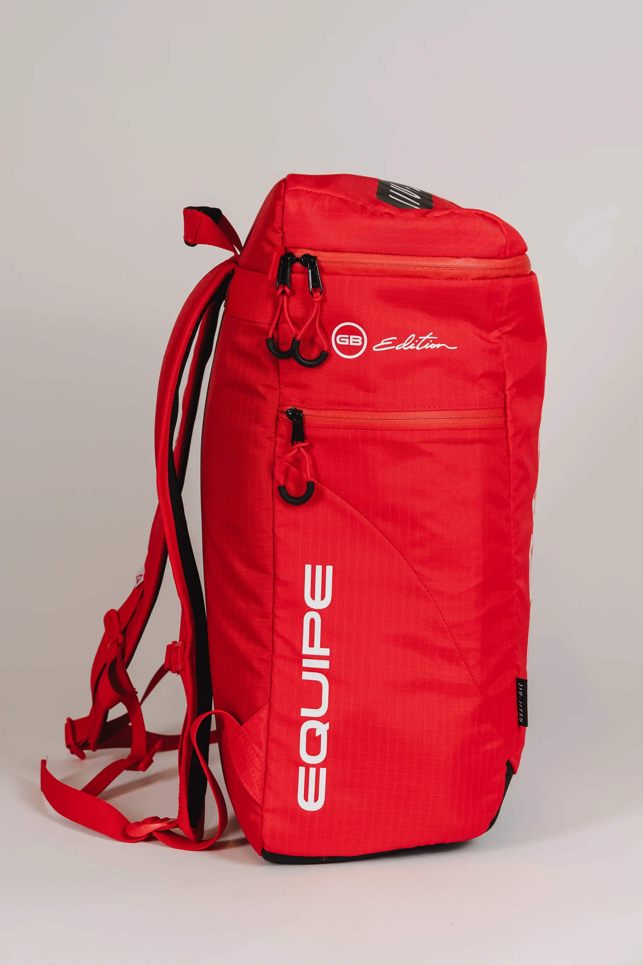 Side view of Red Comp GB4 Backpack from Gracie Barra’s Red Comp Collection showing “Equipe” and “GB Edition” logos with red straps and ventilation pocket.