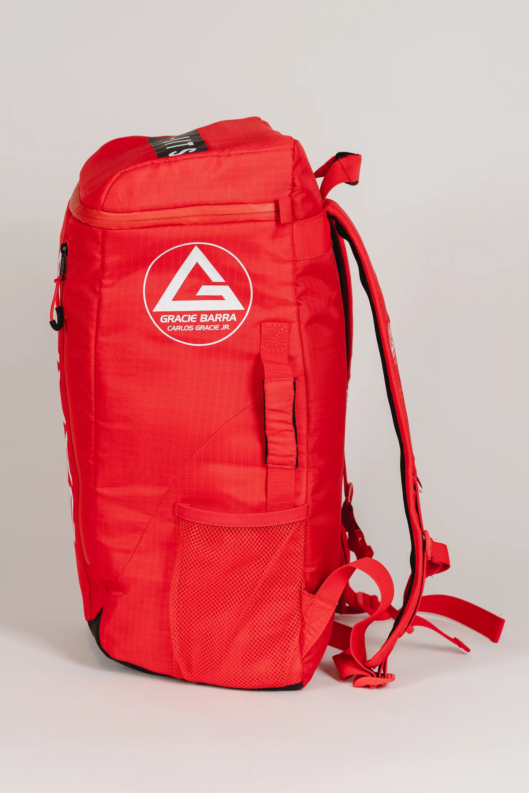Side profile of Red Comp GB4 Backpack featuring the Gracie Barra shield logo, mesh side pocket, and ergonomic red straps from the official Red Comp Collection.