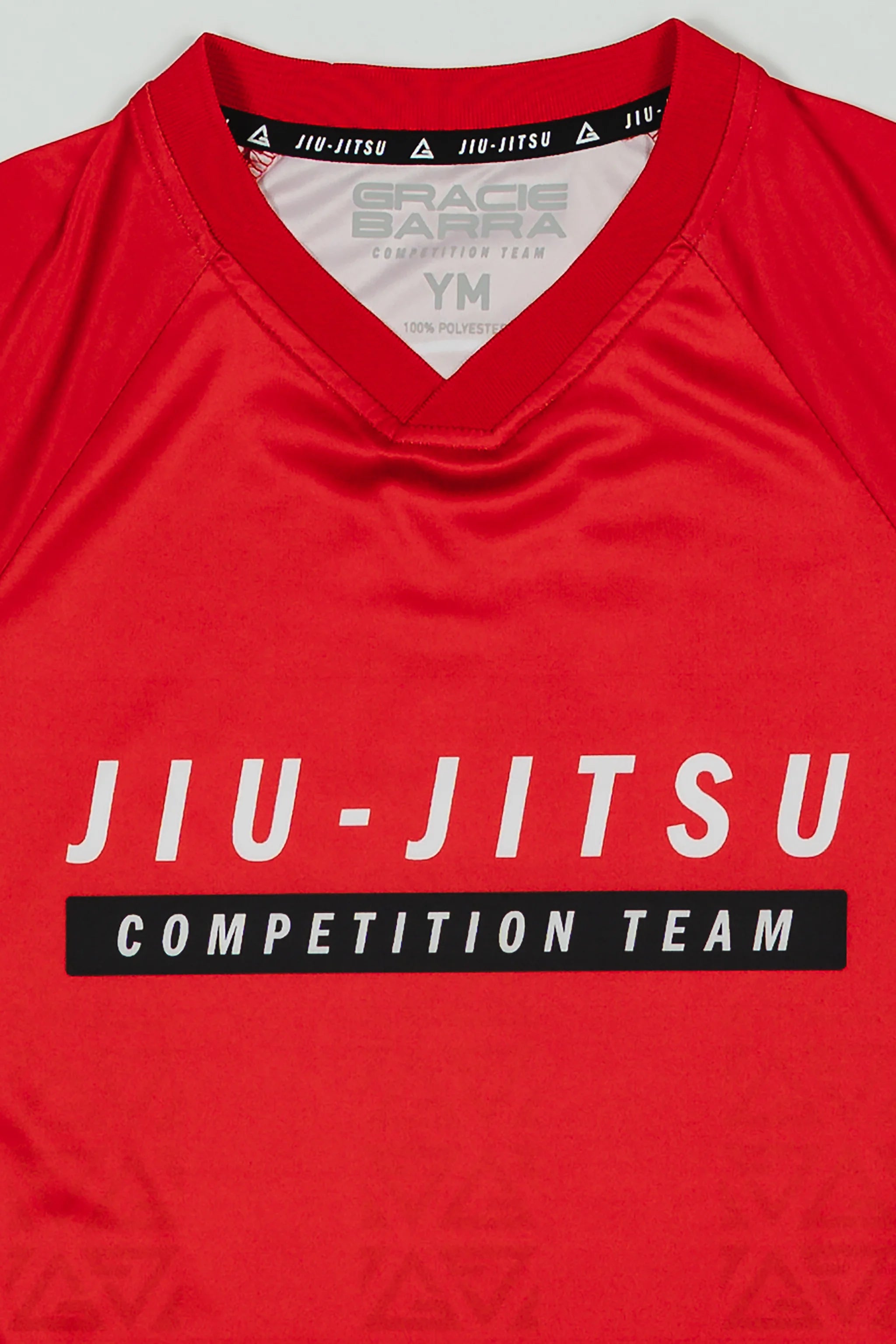 Close-up of the Kids’ Red Comp Team Jersey showing the official Jiu-Jitsu Competition Team front graphic and collar details with inner Gracie Barra branding.