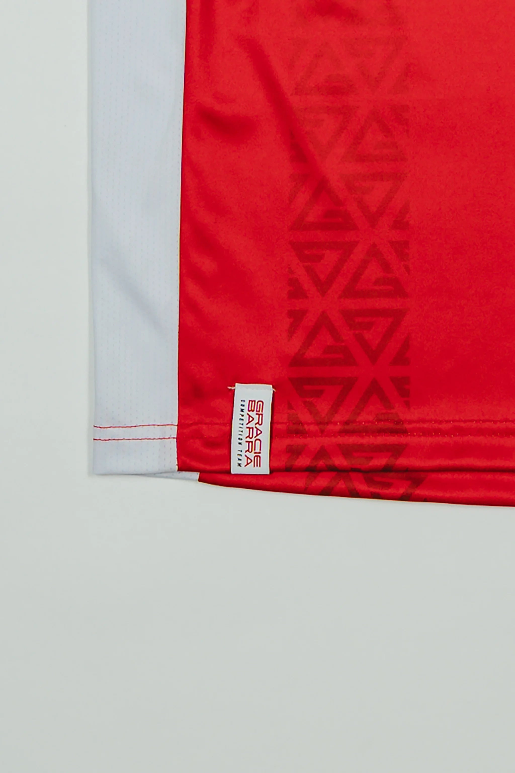 Close-up of the Kids’ Red Comp Team Jersey showing the tonal Legacy G geometric pattern and woven Gracie Barra Competition Team label above the hem.