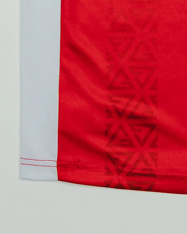 Close-up of the Kids’ Red Comp Team Jersey hem highlighting the Legacy G geometric pattern and white side panel.