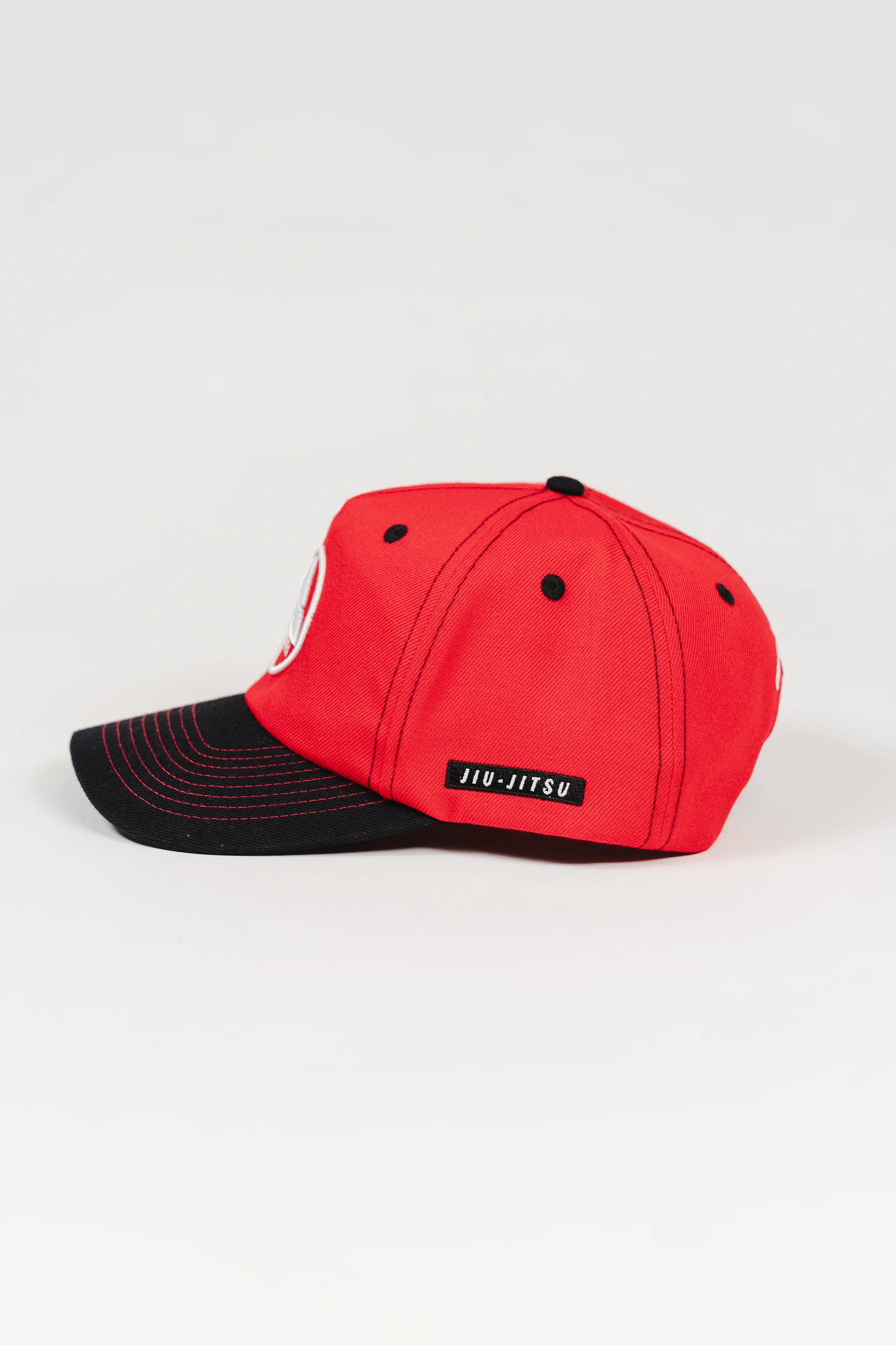 Side view of the Red Comp Team Cap showing the black brim, GB Red crown, and woven JIU-JITSU label above the side seam.