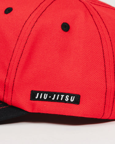 Close-up of the Red Comp Team Cap showing the woven black JIU-JITSU label stitched onto the GB Red wool twill side panel with black eyelets and stitching.