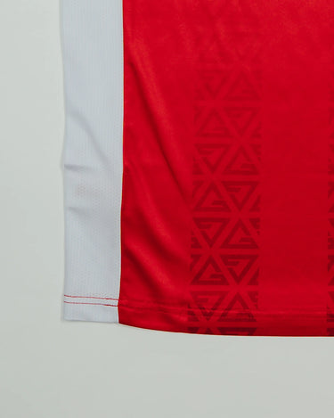 Close-up of the Men’s Red Comp Team Jersey hem showing the tonal Legacy G geometric pattern and white side panel detail.
