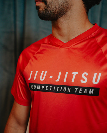 Close-up of Professor Ian wearing the Men’s Red Comp Team Jersey, highlighting the official Jiu-Jitsu Competition Team front graphic and V-neck collar detail.