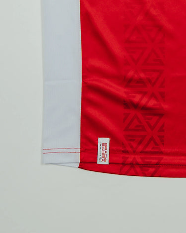 Close-up of the Men’s Red Comp Team Jersey hem showing the tonal Legacy G geometric pattern, white mesh side panel, and woven Gracie Barra Competition Team label.