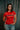 Professor Keanna wearing the Red Comp Women’s Team Jersey featuring the official Jiu-Jitsu Competition Team graphic, photographed against a dark backdrop.