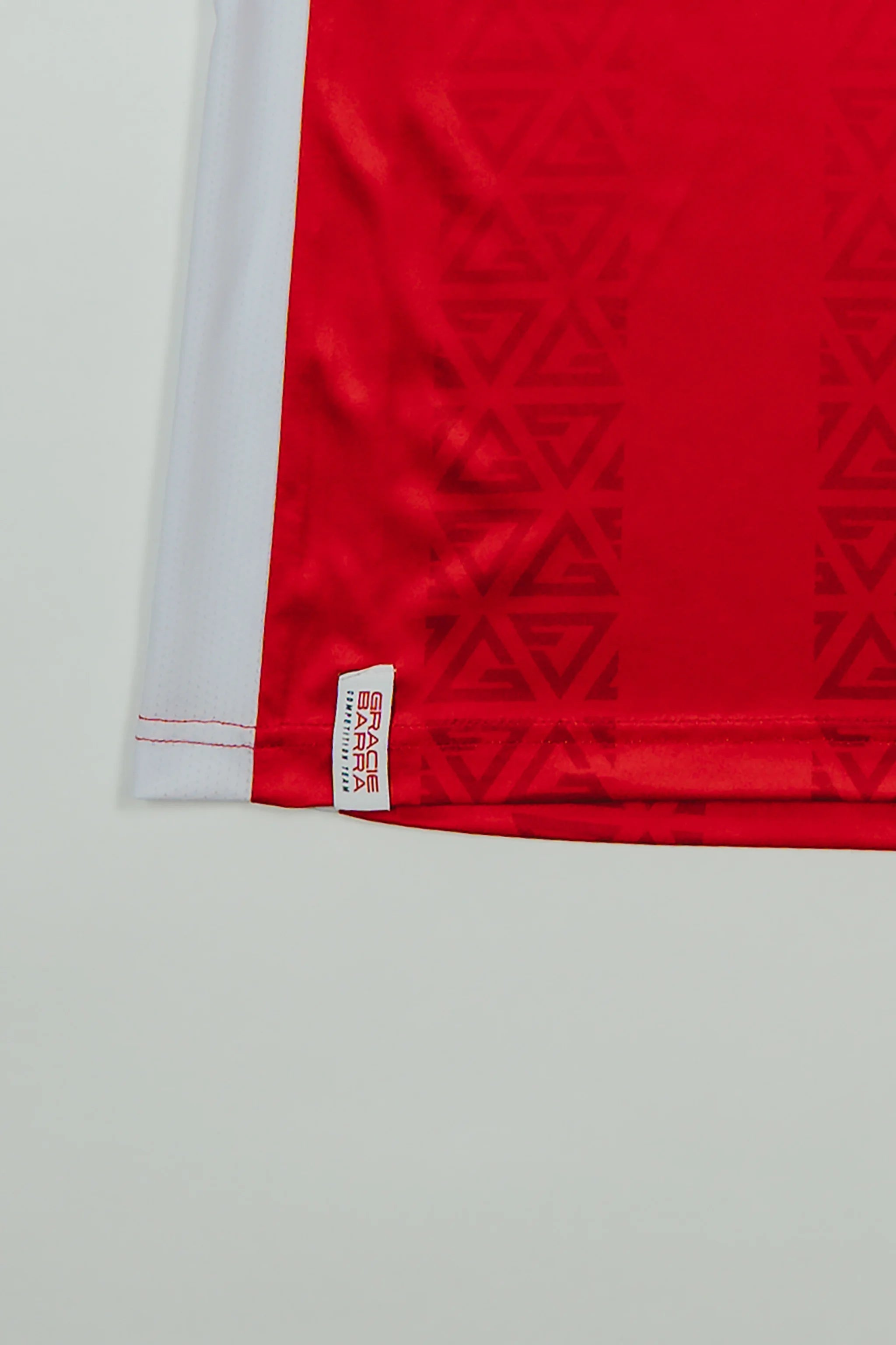 Close-up of Red Comp Women’s Team Jersey showing tonal GB Red pattern and woven Gracie Barra stacked logo label above the hem.
