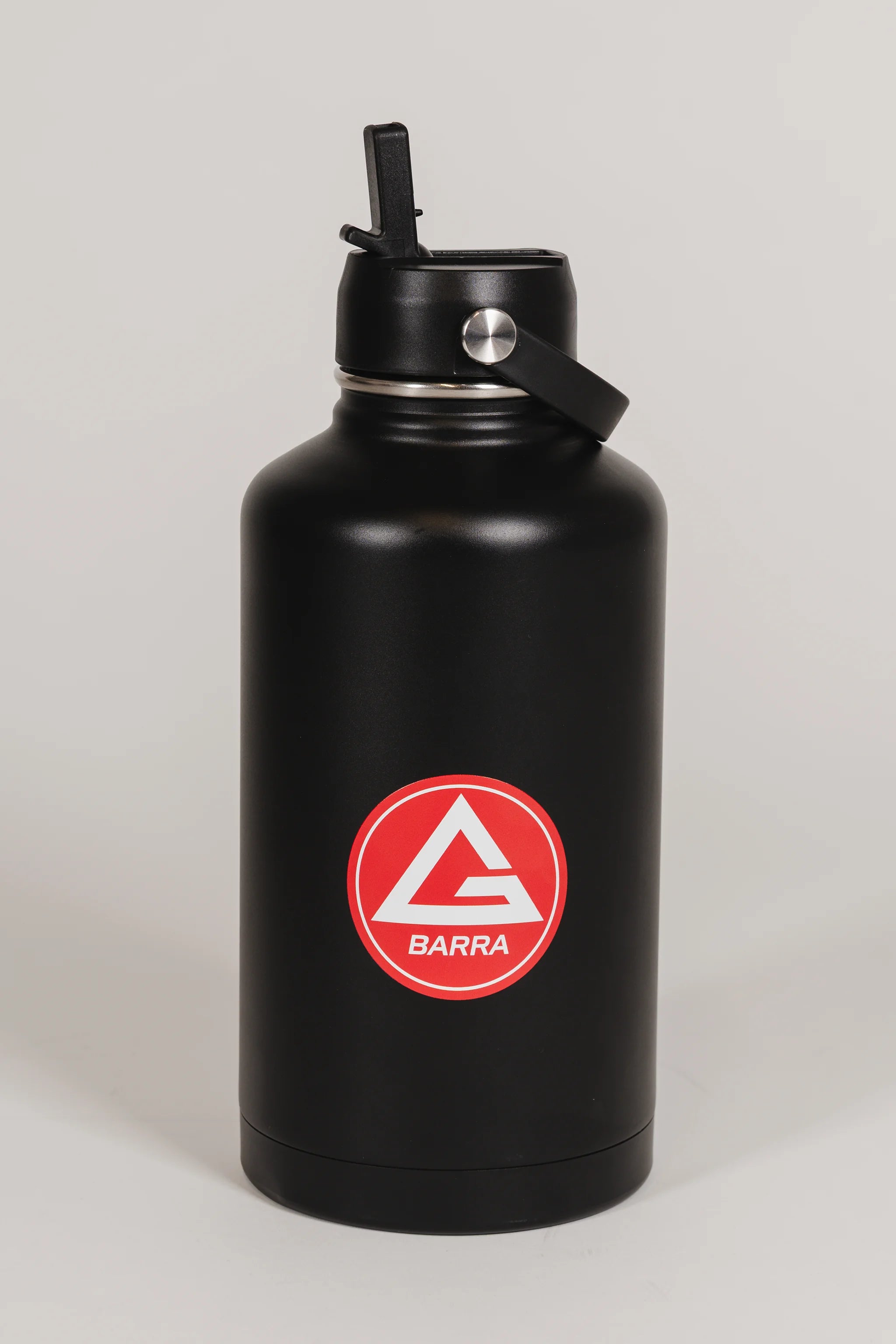 Black stainless steel 64 oz Red Shield bottle with the Gracie Barra Red Shield logo on the front, shown with the straw lid open, photographed against a light background.