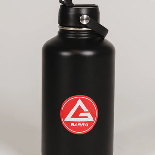 Black stainless steel 64 oz Red Shield bottle with the Gracie Barra Red Shield logo on the front, shown with the straw lid open, photographed against a light background.