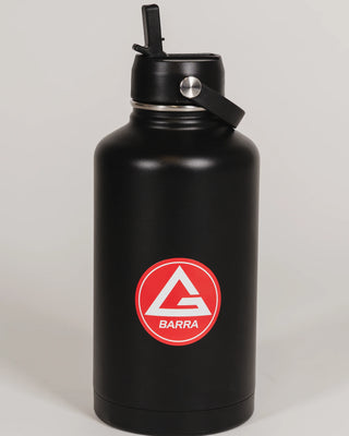 Black stainless steel 64 oz Red Shield bottle with the Gracie Barra Red Shield logo on the front, shown with the straw lid open, photographed against a light background.