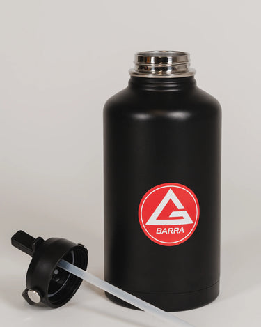 Black stainless steel 64 oz Red Shield bottle with the Gracie Barra Red Shield logo, shown with the straw lid removed and placed in front of the bottle, photographed against a light background.