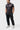 Student in the black Red Shield Terra Mar polo, full length front view turned slightly to the side, hands in pockets.